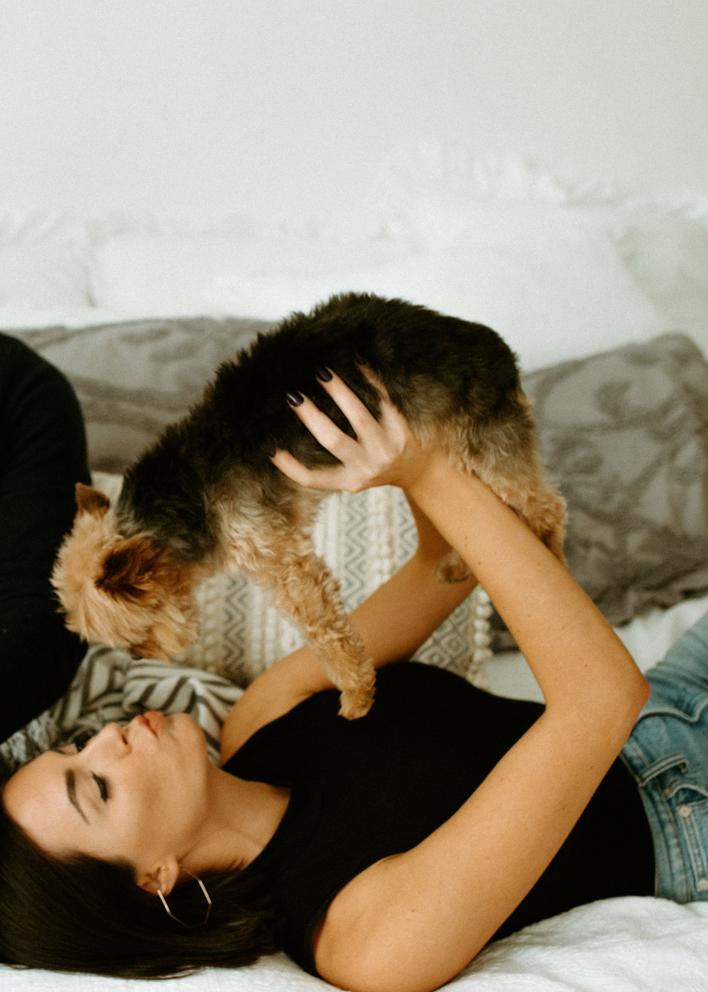 woman on bed holding her small dog above her head.